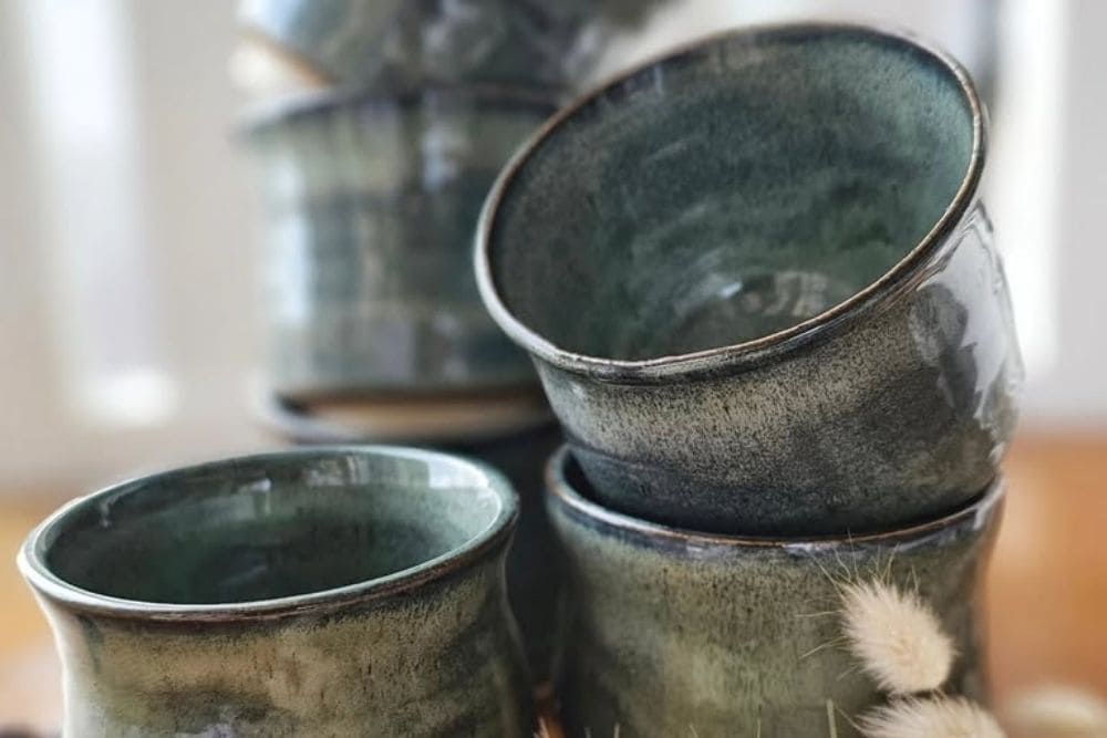 Handcrafted mottled green ceramic cups stacked neatly on a wooden surface-